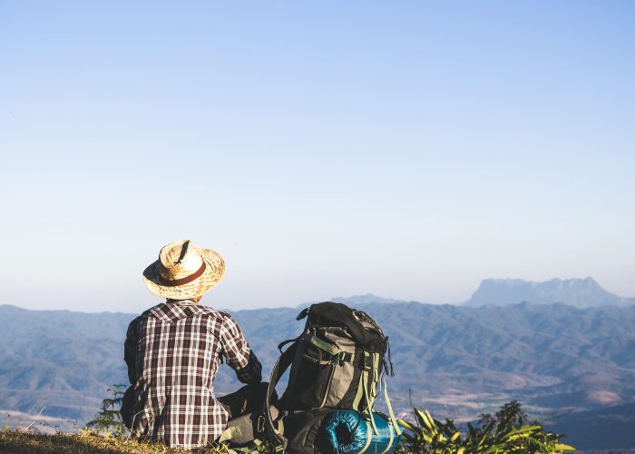 Tourist from mountain top. sun rays. man wear big backpack against sun light